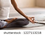 Yogi black woman practicing yoga lesson, breathing, meditating, doing Ardha Padmasana exercise, Half Lotus pose with mudra gesture, working out, indoor close up. Well being, wellness concept
