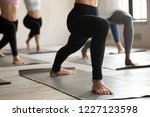 Group of young sporty people practicing yoga lesson, doing Warrior one pose, Virabhadrasana 1 exercise, working out, indoor close up, students training at club or yoga studio. Leg stretching concept