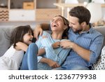 Cheerful people sitting on couch in living room have fun little daughter tickling mother laughing together with parents enjoy free time playing at home. Weekend activity happy family lifestyle concept