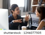 Friendly female colleagues having good relationships, pleasant conversation at workplace during coffee break, smiling young woman listen talkative coworker, discussing new project, talking in office