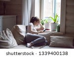 Woman upset after reading bad message on phone at home. Frustrated sad female crying, suffering, not in mood, thinking, depressed, stressed sitting on comfortable sofa near window holding smartphone