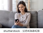 Woman sitting on sofa at home looks at smartphone device screen listens song choose online audio book make call or watching music videos. Teenage girl having fun spending free time in internet concept