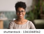 Head shot portrait of happy mixed race girl wearing glasses, smiling african american millennial woman posing indoor, pretty positive female student businesswoman young professional looking at camera
