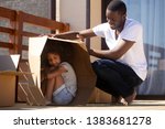 Young African American dad play with small daughter outside new house on moving day, black millennial father have fun with little kid, hiding in cardboard box enjoy relocating to own home
