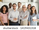 Smiling multiethnic employees standing looking at camera making team picture in office together, happy diverse work group or department laugh posing for photo at workplace, show unity and cooperation