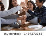 Overjoyed diverse multiracial young people stack fists engaged in funny teambuilding activity at group meeting, excited multiethnic students build strong cooperation show unity support at gathering