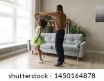 Small photo of Young african American father dance together with happy preschooler daughter wearing ballet skirt, happy black dad sway swirl excited biracial girl child dancer in green dress in living room at home