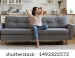 In cozy living room happy woman put hands behind head sitting leaned on couch 30s european female enjoy lazy weekend or vacation, housewife relaxing feels satisfied accomplish chores housework concept