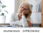 Small photo of Exhausted aged woman worker sit at office desk fall asleep distracted from work, tired senior businesswoman feel fatigue sleeping at workplace taking break dreaming or visualizing