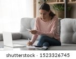 Small photo of Serious young woman calculating counting vat paying domestic bills writing notes at home, focused female renter do paperwork planning expenses using calculator laptop managing finances sit on sofa