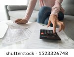 Woman renter holding paper bills using calculator for business financial accounting calculate money bank loan rent payments manage expenses finances taxes doing paperwork concept, close up view