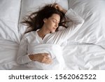 Peaceful serene beautiful young lady wear pajamas lying asleep relaxing sleeping in cozy white bed on soft pillow resting covered with blanket enjoying good healthy sleep concept, above top view