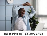 Tired african American male worker yawn stretch in office chair overwhelmed with work at workplace, exhausted biracial young man employee sign feel fatigue after long day, having sleep deprivation