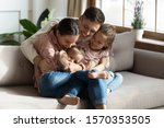 Happy cheerful parents having fun with cute children daughters cuddling playing on sofa together, mom and dad laughing embracing little kids daughters tickling enjoying family lifestyle games at home