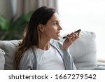 Young Caucasian woman sit on couch in living room using smartphone activate virtual digital assistant, millennial girl record voice message on modern cellphone gadget, new technology concept