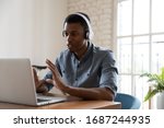 Small photo of Serious confident African manager wear headphones looking at laptop screen talking provide support to client distantly, convincing customer buy company services. Student and e-learning process concept