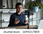 Small photo of Smiling indian ethnic girl sitting in front of smartphone on stabilizer, recording self-presentation video or sharing professional skills. Happy young smart businesswoman filming educational lecture.