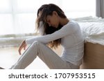 Unhappy woman touching hair, sitting on floor at home, thinking about problems, upset girl feeling lonely and sad, psychological and mental troubles, suffering from bad relationship or break up