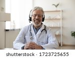 Smiling senior old doctor wears headset looking at camera. Remote online medical chat consultation, tele medicine distance services, virtual physician conference call, telemedicine concept. Portrait.