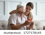 Small photo of Smiling millennial girl close cover mature father eyes make birthday surprise congratulate at home, loving grownup adult daughter greeting beloved happy senior dad, give wrapped gift box present