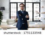 Portrait of smiling successful Caucasian businessman in formal suit glasses stand posing in modern office, happy young male boss or CEO look at camera, show confidence and power, leadership concept