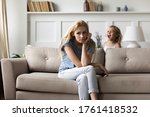 Small photo of Screaming noisy little daughter brings mom to despair, parent feels tired resting seated on couch in living room. Hyperactive and naughty disobedient child, omission in upbringing or nurture concept