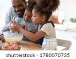 Loving african american father make dough making tasty sweet breakfast pastry with excited little children, happy biracial dad and small kids cook prepare pancakes cookies pie in kitchen together