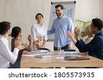 Smiling male leader praising happy millennial arab colleague at group meeting. Smiling diverse coworkers applauding, supporting new worker or congratulating with personal professional achievement.