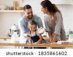 Happy parents with adorable little daughter having fun with dough, baking pastry or pie together, laughing father clapping hands with flour, overjoyed family enjoying leisure time in kitchen