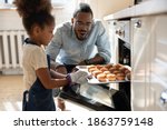 Small photo of Wow, looks great! Excited caring millennial african dad or grown elder brother watching concentrated small black daughter or younger preteen sister taking pan with self baked tasty muffins out of oven
