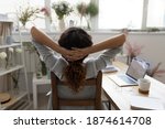 When all is done. Back rear view of happy young female florist sitting on chair in cozy studio pleased with work results. Creative interior designer stretching with hands behind head resting relaxing