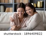Close up smiling mature mother embracing grownup daughter, having fun, sitting on cozy couch at home, happy young woman with elderly mum enjoying leisure time together, excited by good news