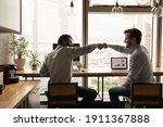Small photo of Well done, buddy. Motivated diverse young men coworkers bump fists on workplace feel excited achieve common goal. Two workers international business team members share success glad to help one another