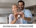 Close up focus of happy young Caucasian couple show keys to first share own apartment or house. Smiling millennial man and woman celebrate relocation to new home. Moving, rental, estate concept.
