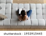 Spending leisure time. Top view of casual female student teenager sit on comfortable couch at living room read book with blank pages. Young woman looking through photo album choose goods in catalogue