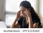 Small photo of What should I do. Stressed latina woman sit by pc rub temples feel information overload unable to focus attention on work. Anxious young female try to remember important thing solve unexpected problem