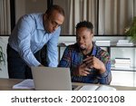 African American mentor teaching intern, pointing at laptop screen, executive manager leader instructing new employee, explaining strategy, colleagues working on online project in office together