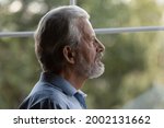 Sad pensive older senior 70s man lost in thoughts looking out window, suffering from memory loss, dementia, Alzheimer disease, feeling loneliness. Old age problems, elderly healthcare concept