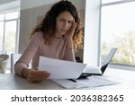 Small photo of Nervous unhappy young hispanic woman looking through paper document, feeling stressed of getting bank loan rejection notification or job dismissal notice, having financial problems, bankruptcy concept