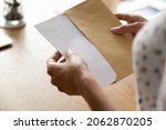 Small photo of Hands of woman receiving letter, invitation, notification, postcard, taking out document for reading, opening envelope with blank folded paper at work desk. Mail concept. Close up, cropped shot