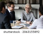 Businesspeople group of diverse gender generation hold negotiations at conference table. Business partners shareholders meet at boardroom discuss work on new project talk about profitable investments