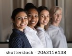 Small photo of Multi ethnic group of successful confident women office workers professional experts stand in row one after another look at camera. Selective focus on young indian female team leader headshot portrait