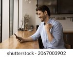 Small photo of Side view happy emotional young caucasian man celebrating online lottery gambling auction giveaway win, getting victory notification on cellphone, feeling joyful sitting at table in modern kitchen.