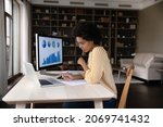 Small photo of Concentrated young African American businesswoman employee worker in eyeglasses analyzing online sales statistics data on computer, reviewing marketing research, working with documents at home office.
