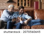 Small photo of Funny playtime. Joyful elderly grandfather millennial dad tickle giggling tween kid boy on couch enjoy cute active game. Overjoyed three generation men family laugh aloud relax play have fun together