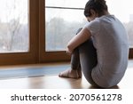 Small photo of Back rear view young miserable unhappy female emb knees seated on floor near window feels lonely, thinks over life concerns, experiences personal troubles, teenager suffers from bullying concept