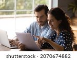 Reading documents. Family couple study papers search information by loan mortgage affordable housing program on website. Young spouses clients hold bank account statement check financial data online