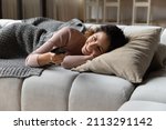 Hispanic young smiling woman lying on couch cushion holds TV remote controller switch channels watch internet television, single 30s female enjoy day off at cozy home. Lifestyle, lazy holidays concept