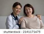 Small photo of Medical care. Headshot portrait of two females young doctor and elderly patient pensioner on appointment at clinic. Happy confident attending physician hug shoulders of mature lady client help support