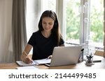 Small photo of Diligent student in headphones makes task sit at desk with laptop, e-learn english, take part in video call with online tutor, listen audio course looks happy enjoy study. Learning using tech concept